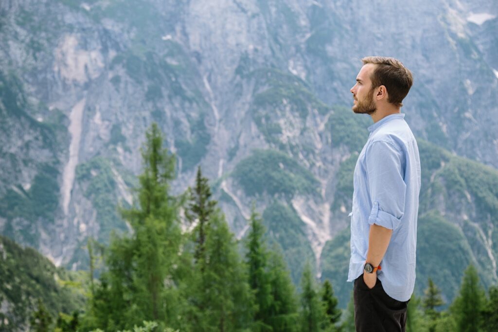 Man standing with hands in pockets, gazing at towering mountain cliffs.