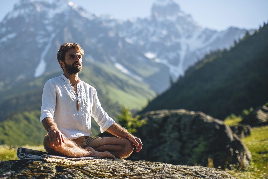 Man meditating on a rock with snow-covered mountains in the background.