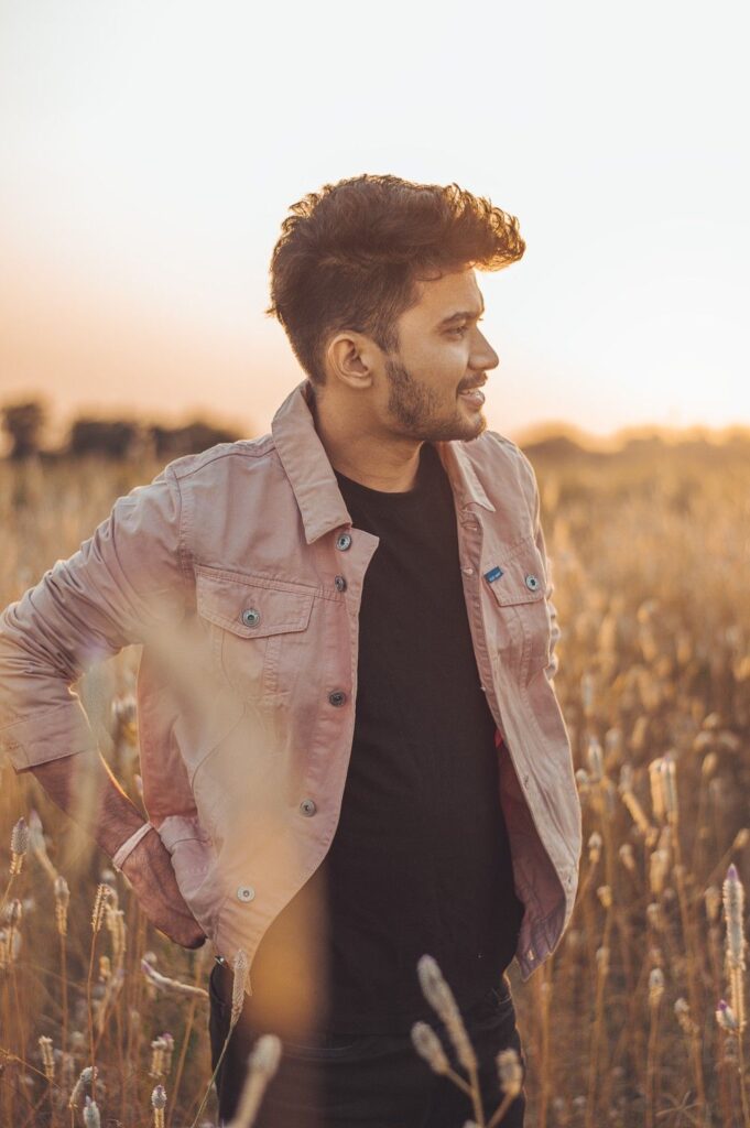 Man in pink jacket standing in golden field at sunset.