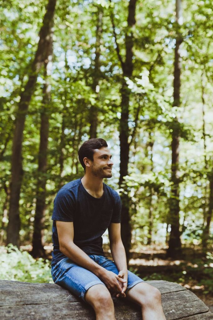Man sitting on a log in the forest, smiling peacefully in sunlight.