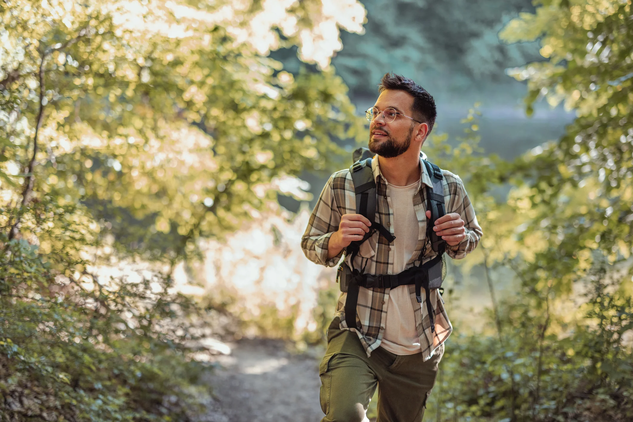 Hiker walking a forest path with sunlight filtering through leafy trees.