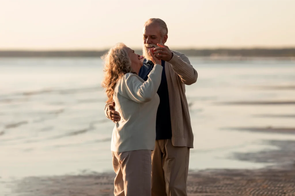 Elderly couple dancing together on the beach during sunset.